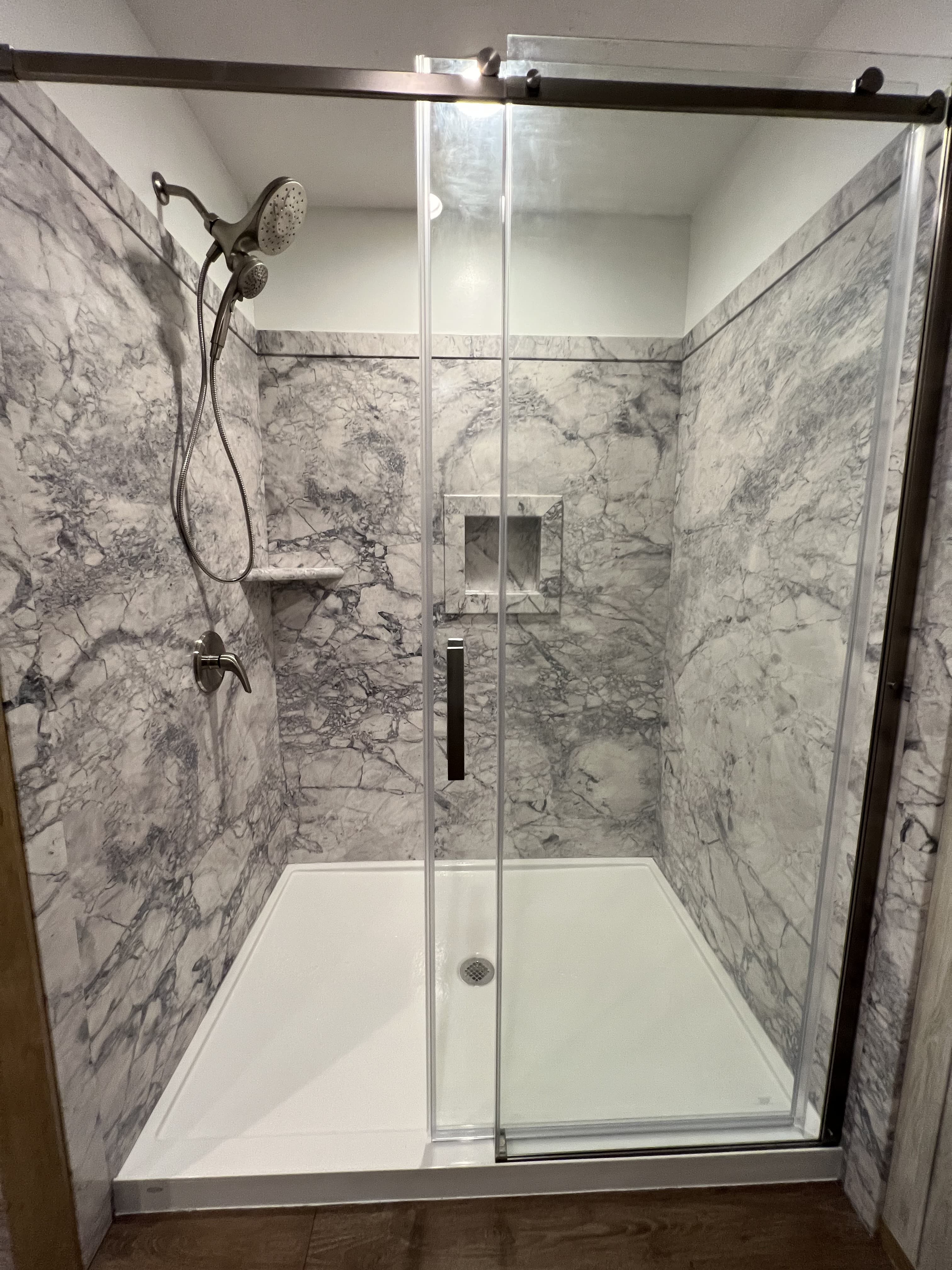 Gray marble walk-in shower with glass sliding doors and a built-in niche