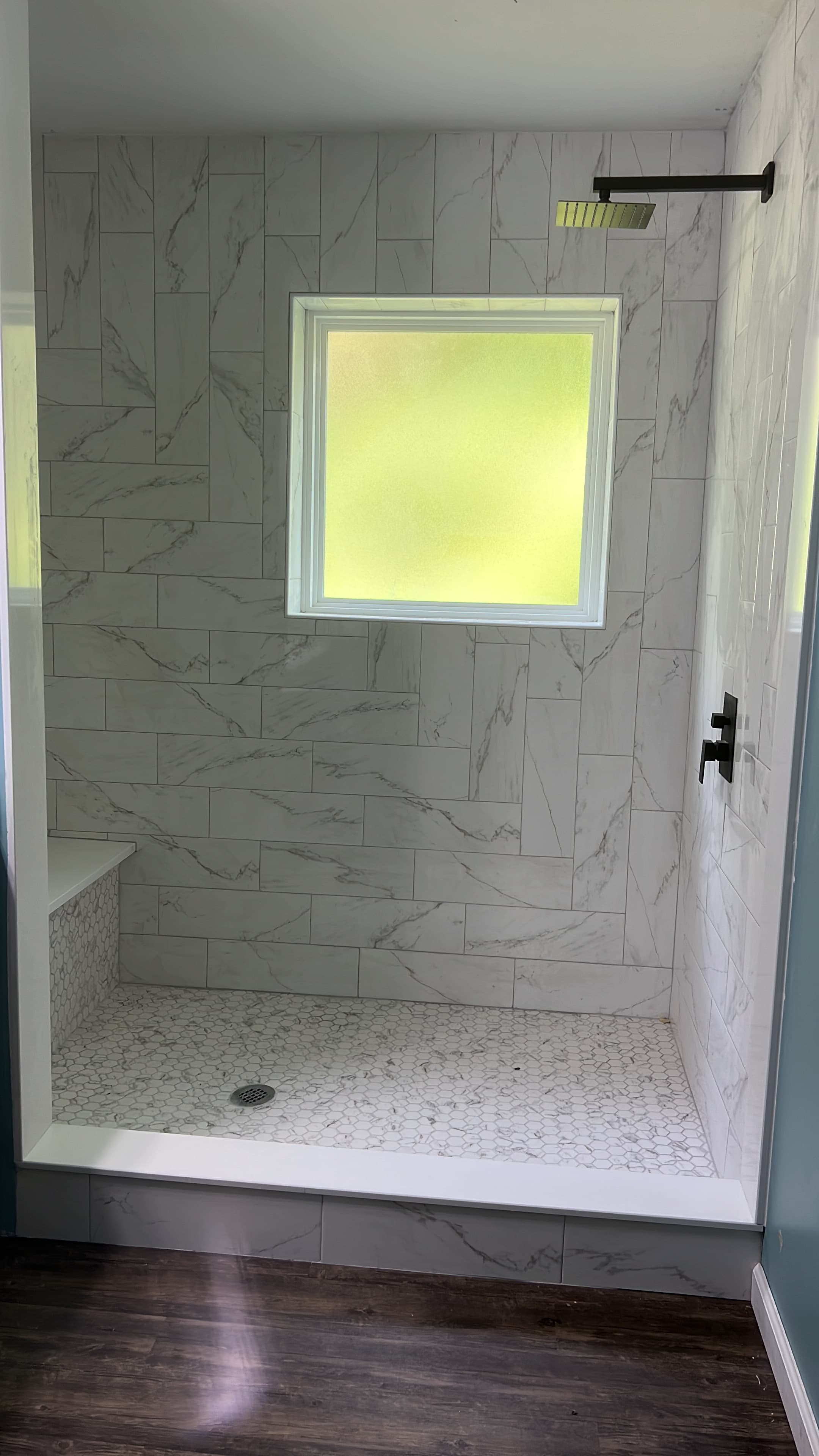 Modern walk-in shower with white marble tile and built-in safety bench