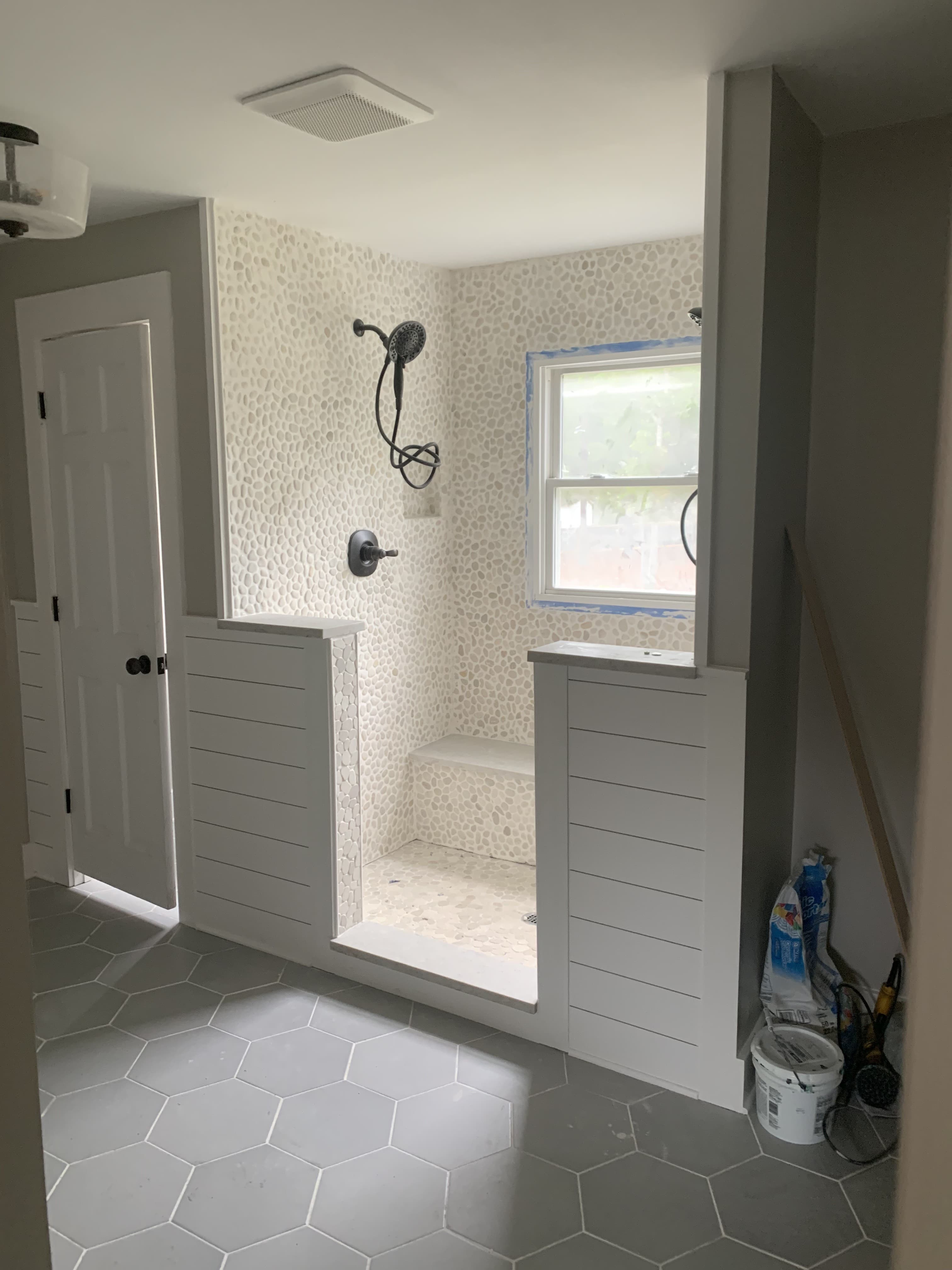 Pebble tile walk-in shower with bench and gray hexagonal floor tile