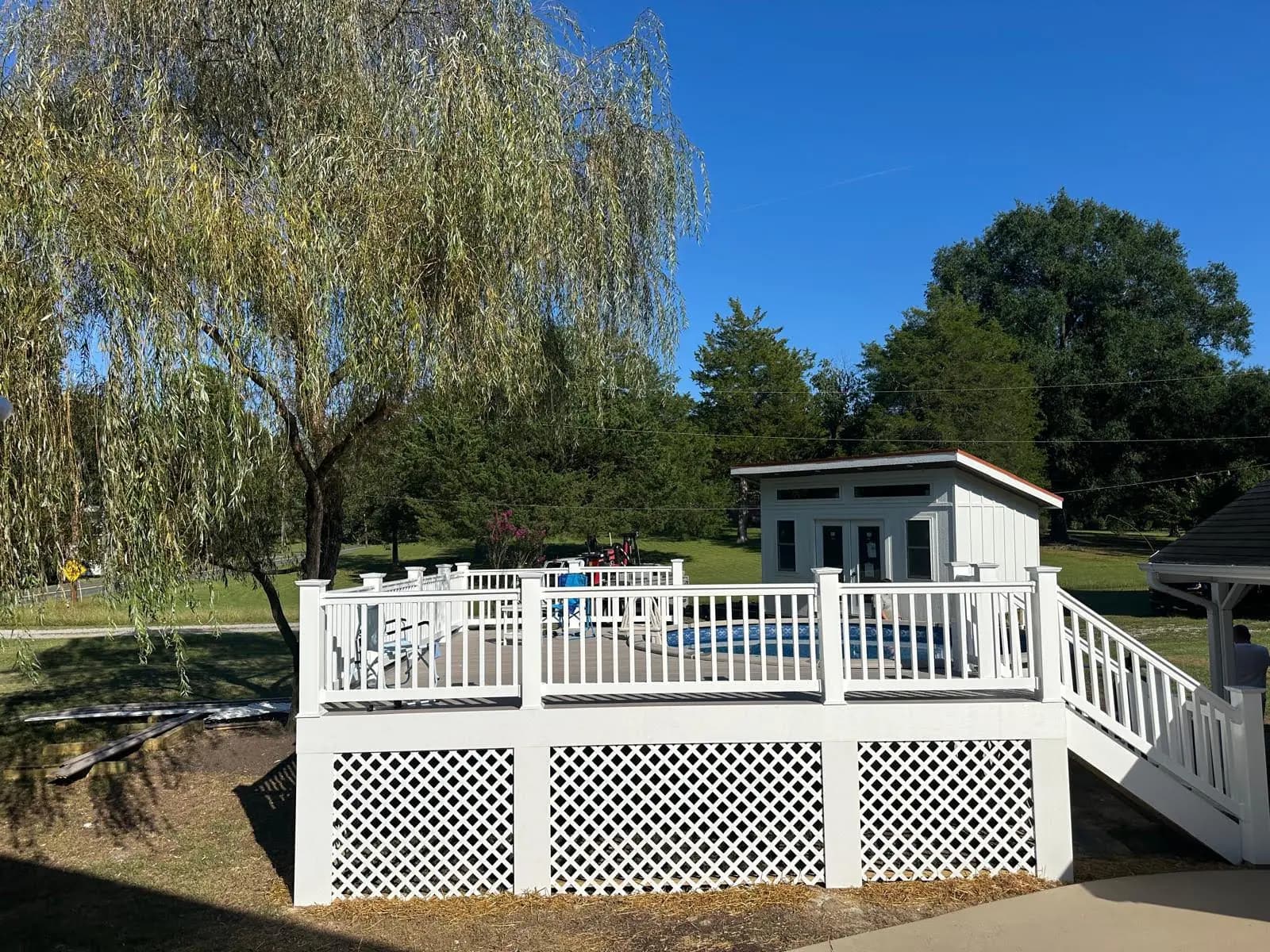 Raised pool deck with white railings, stairs, and white lattice skirting viewed from the yard