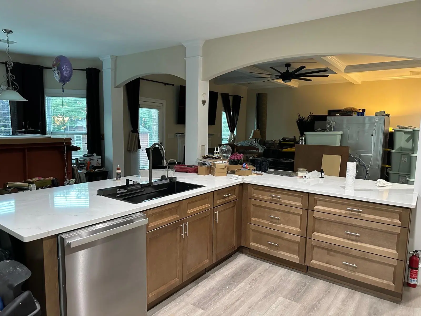 Kitchen renovation in progress with L-shaped white countertops, a black sink, wood base cabinets, and a stainless steel dishwasher