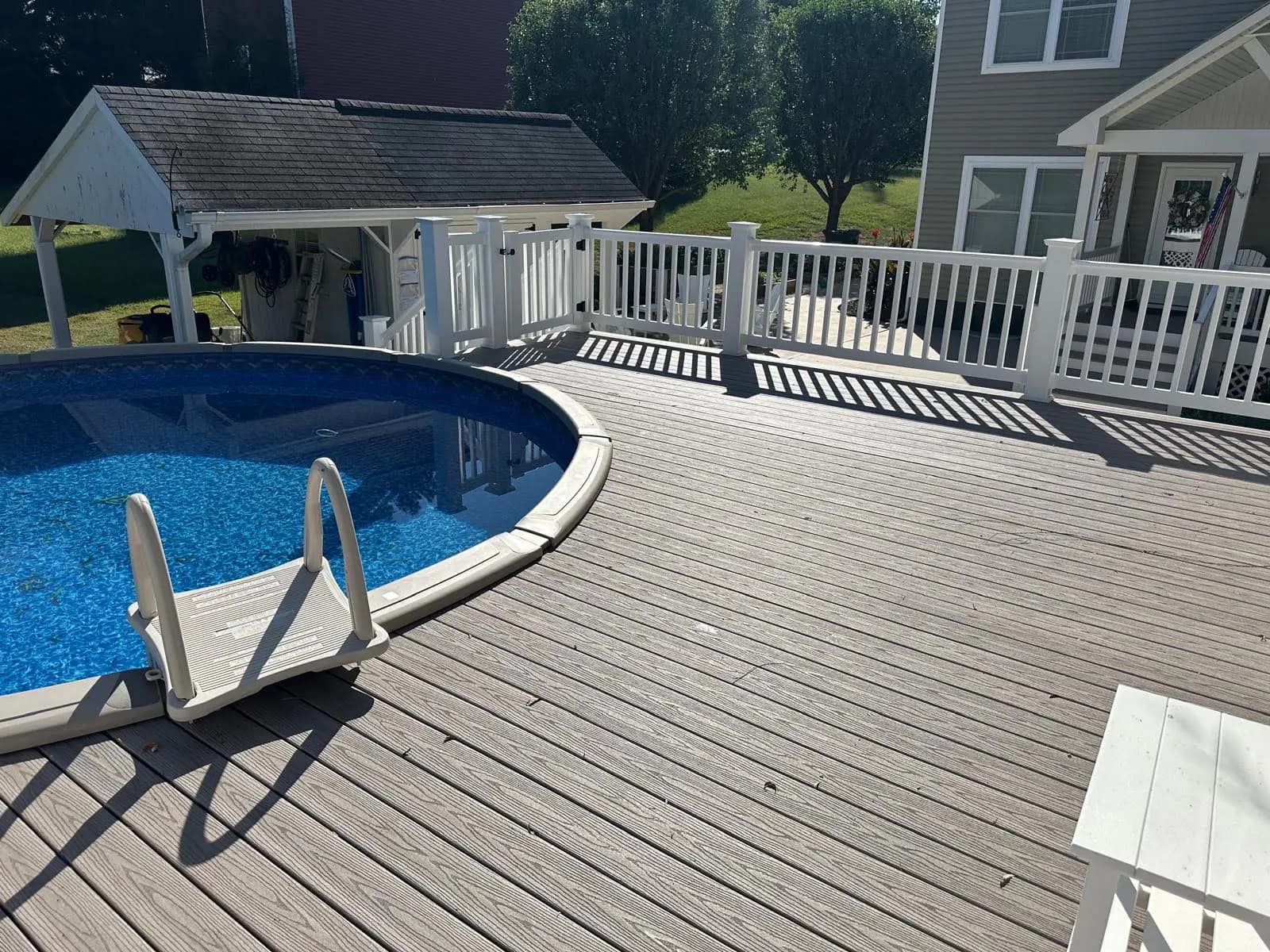 Poolside view of gray decking with white railings and a gate beside the house