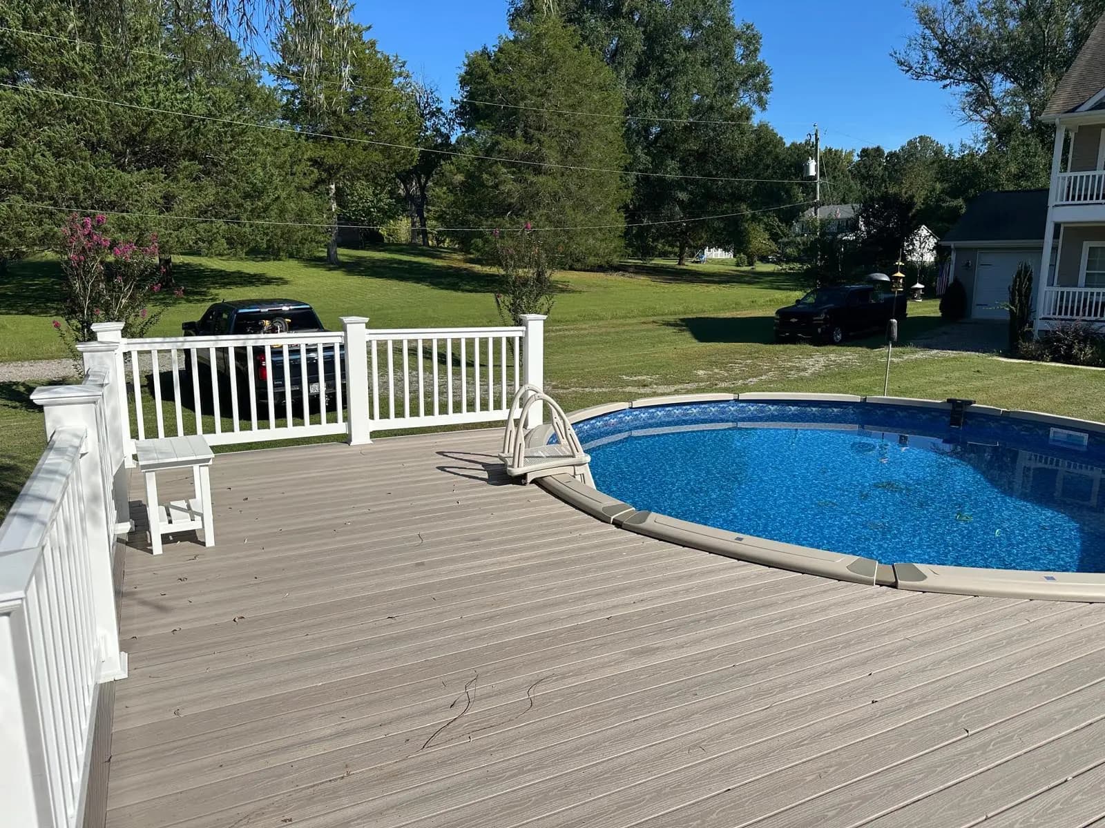 Gray deck boards surrounding an above-ground swimming pool with white railings along the deck edge